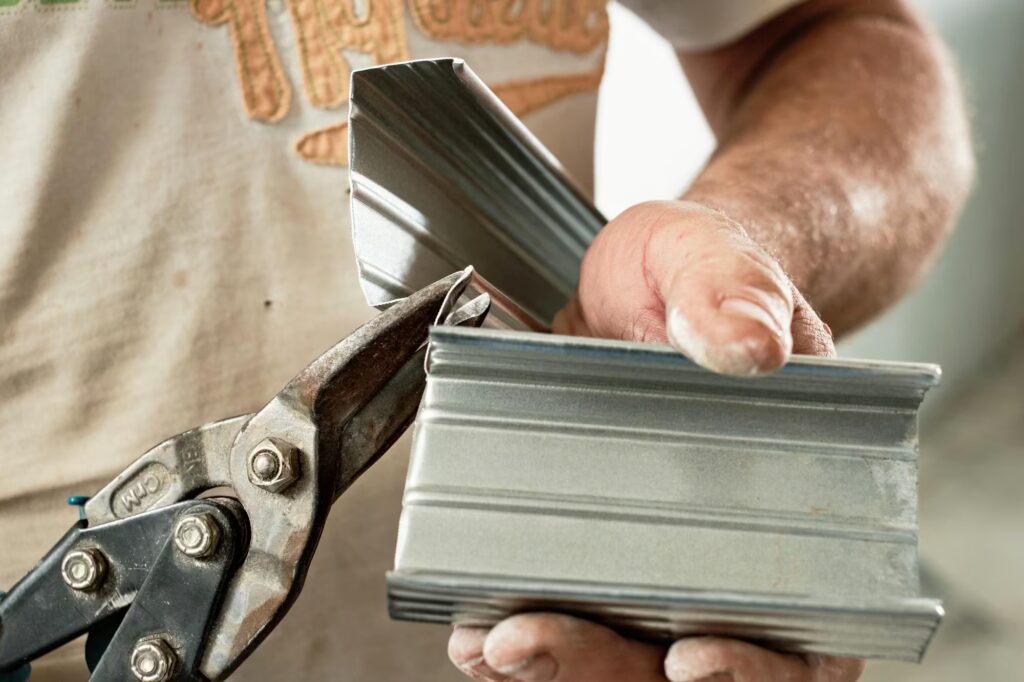 Primer plano de un operario realizando un corte manual con tijeras en un perfil de chapa galvanizada para un ajuste de rematería a medida.
